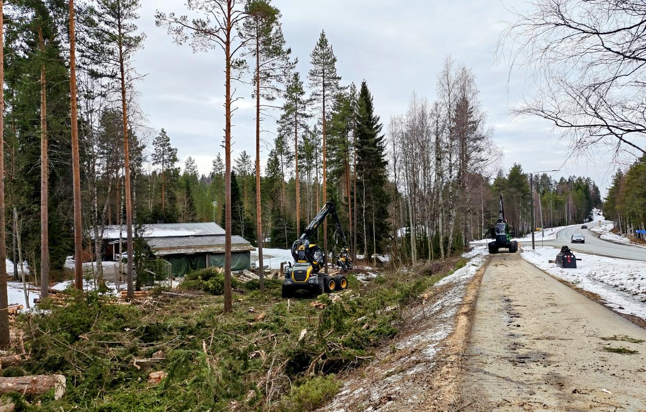 Mets&auml;kone suorittamassa tonttihakkuuta asuinalueen ja tien v&auml;lisell&auml; alueella talvisessa ymp&auml;rist&ouml;ss&auml;